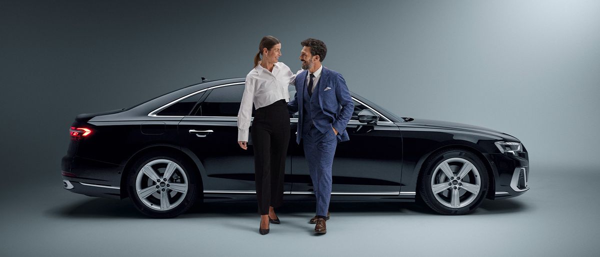 Two coworkers walk arm in arm away from a limousine.